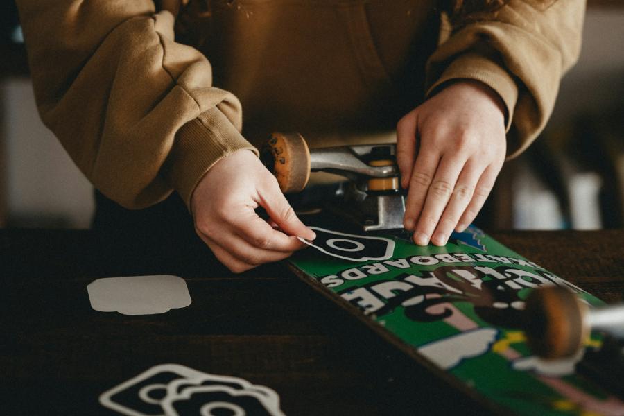 Hands placing stickers on a skateboard deck on a table.