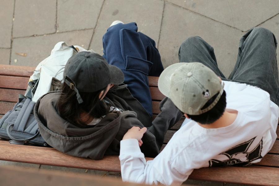 Two people in caps sitting on a bench, seen from above.