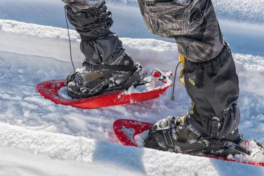 Red snowshoes on snow-covered ground, worn by a person in black pants.