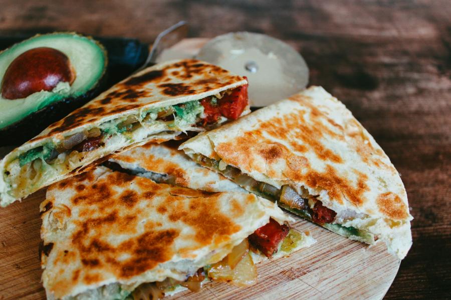 Grilled quesadilla slices on a wooden board, with avocado half nearby.