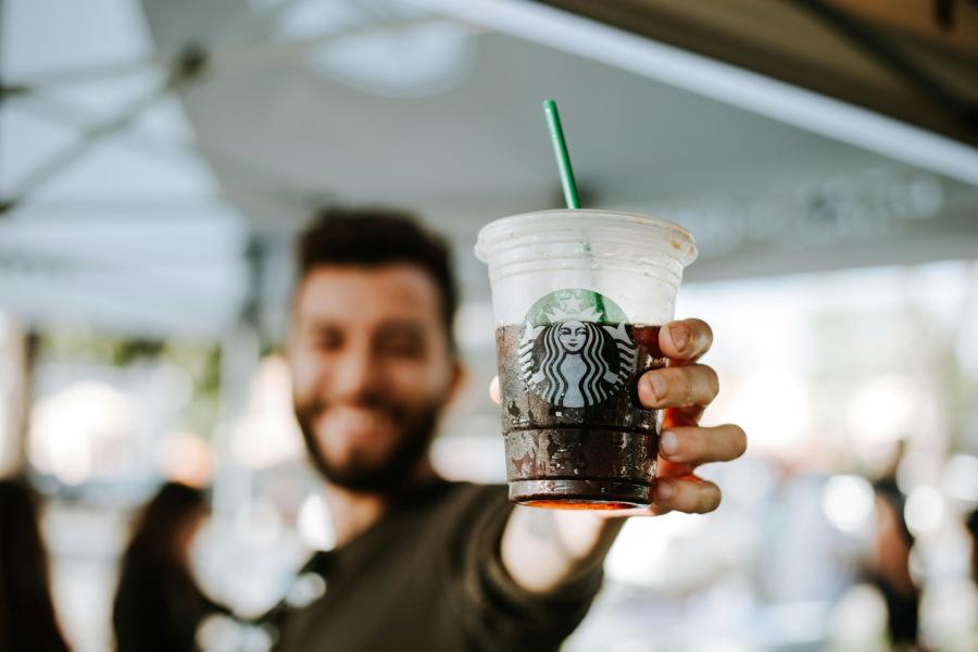 Blurry man smiling, holding iced coffee with straw.