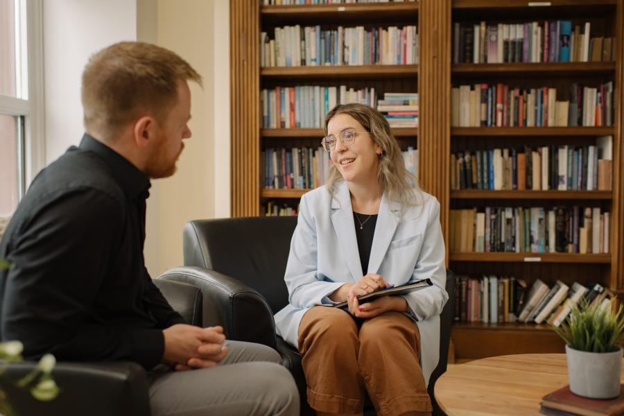 women and man sitting in chairs in front of a bookcase chatting