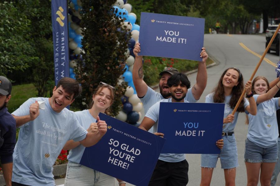 Students and orientation leaders stand along a campus roadway during a TWU orientation event, holding welcome signs and celebrating the arrival of new students on the Langley campus.