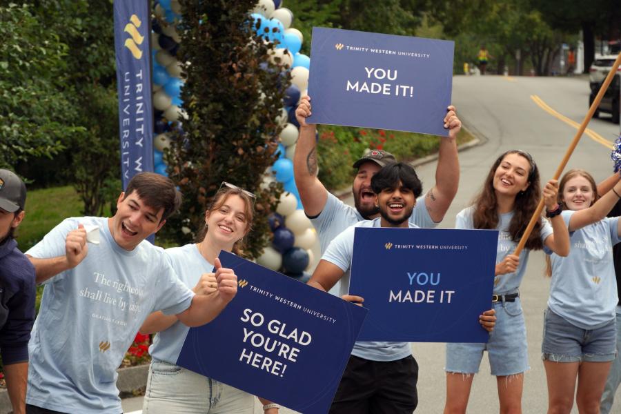 Students and orientation leaders stand along a campus roadway during a TWU orientation event, holding welcome signs and celebrating the arrival of new students on the Langley campus.