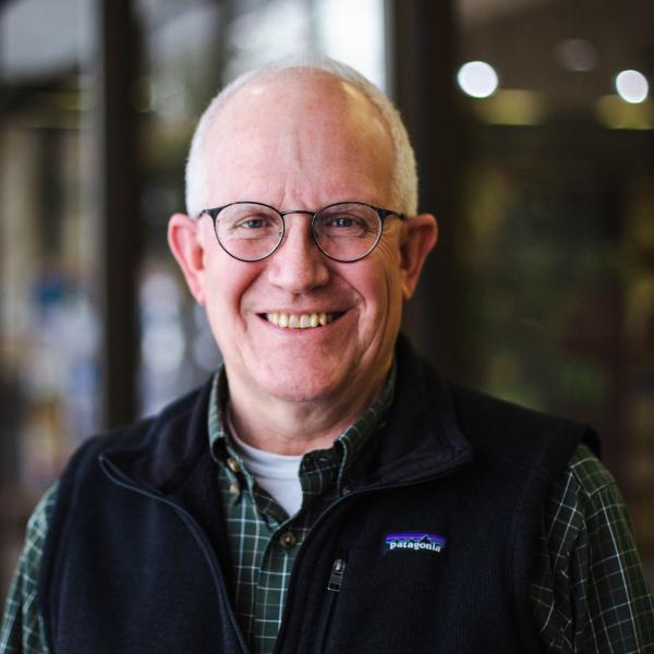 Scott Manetsch in glasses and a vest, standing indoors.
