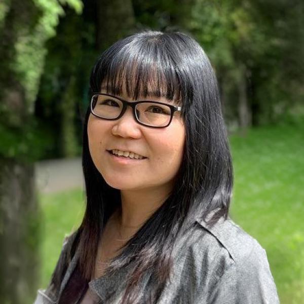 Women with black hair and glasses smiling at the camera in front a green background