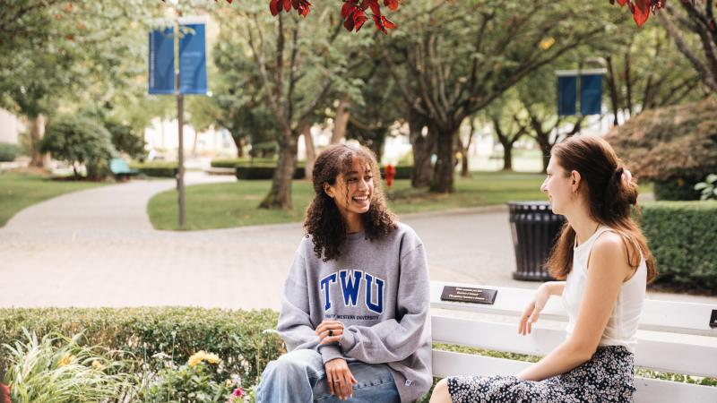 Two female students sitting on a bench talking at the TWU Langley campus.