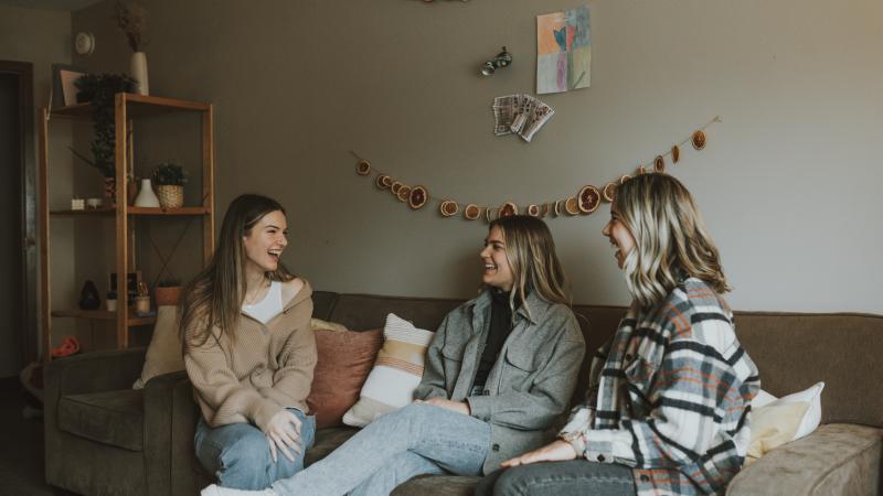 Three female students sitting on a couch in their dorm apartment.