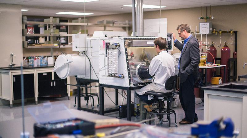 Research lab with student using a machine and professor instructing