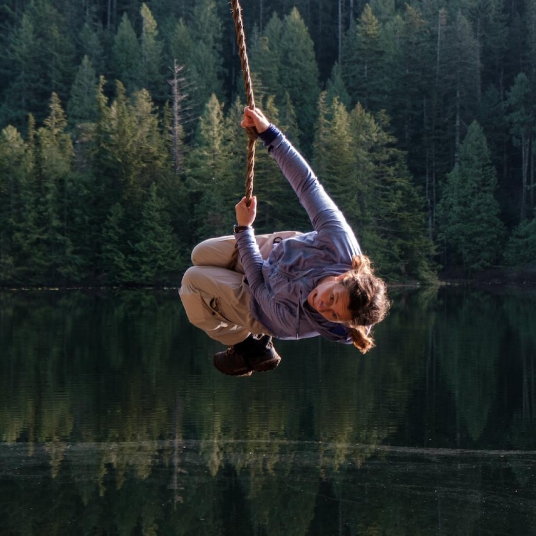 Laura Ginter swinging on a road swing over water with trees behind