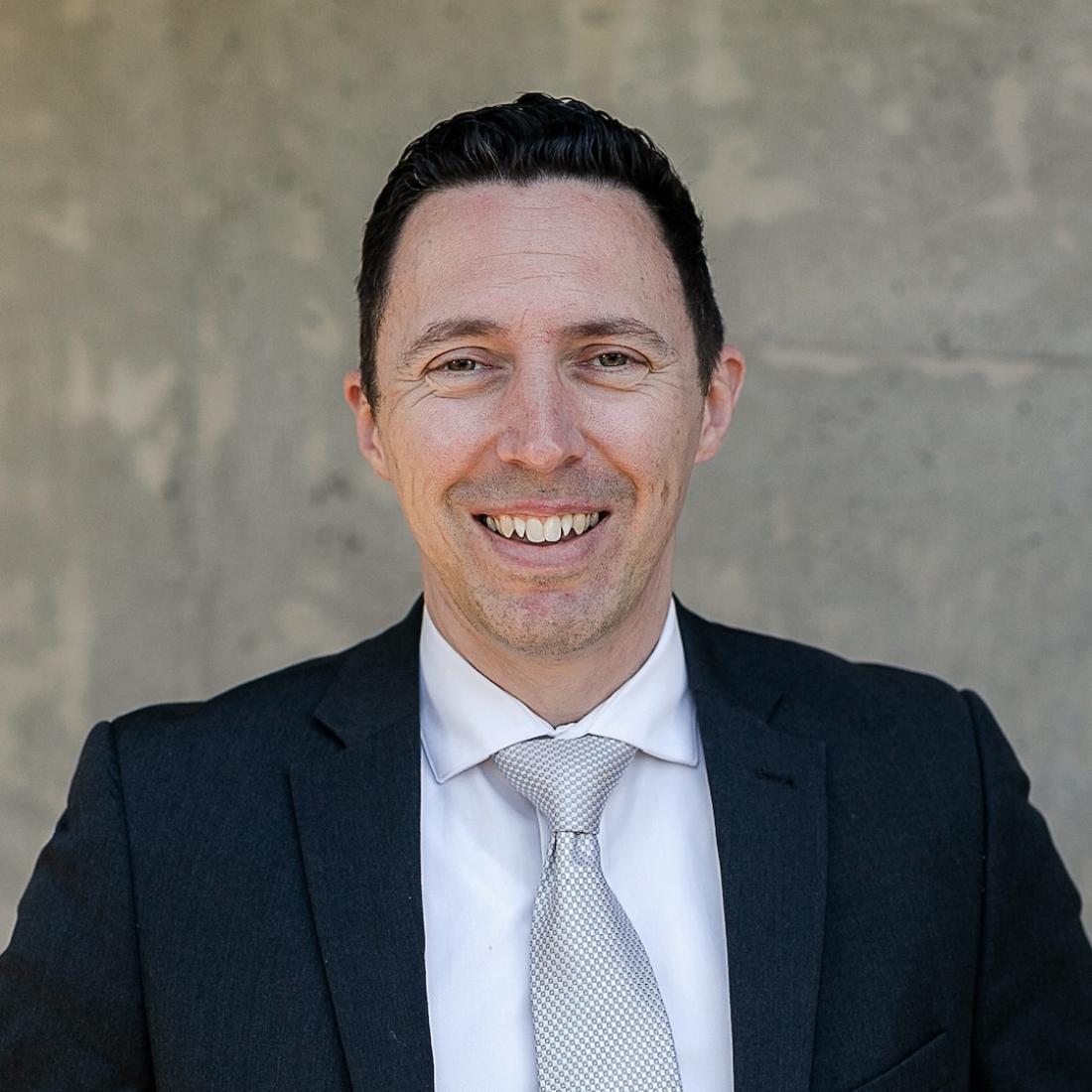 Quentin Fincaryk standing in front of a grey wall in a suit