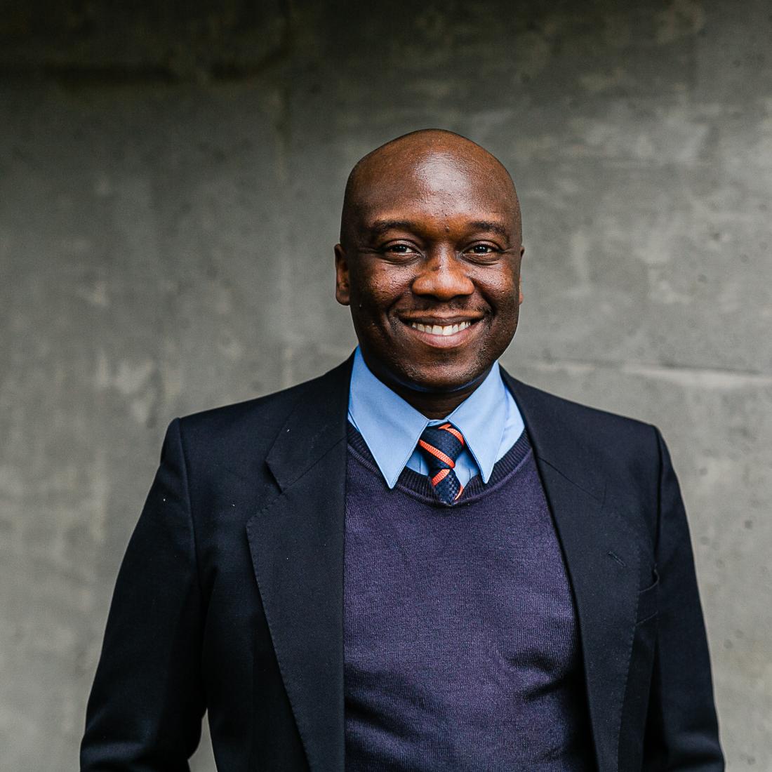 Christopher Ogundare in a suit looking at the camera with a smile on his face