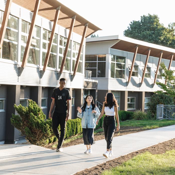 Three students walking on campus outside music building talking.