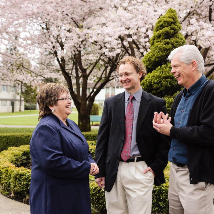 Three people talking outside with greenery and cherry blossom trees