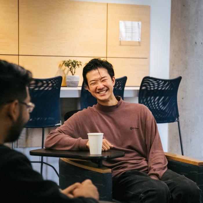 Two males sitting, talking, and smiling over coffee.