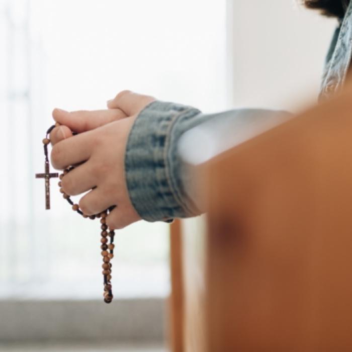 hands holding prayer beads with a cross over a pew in the Catholic Pacific College.