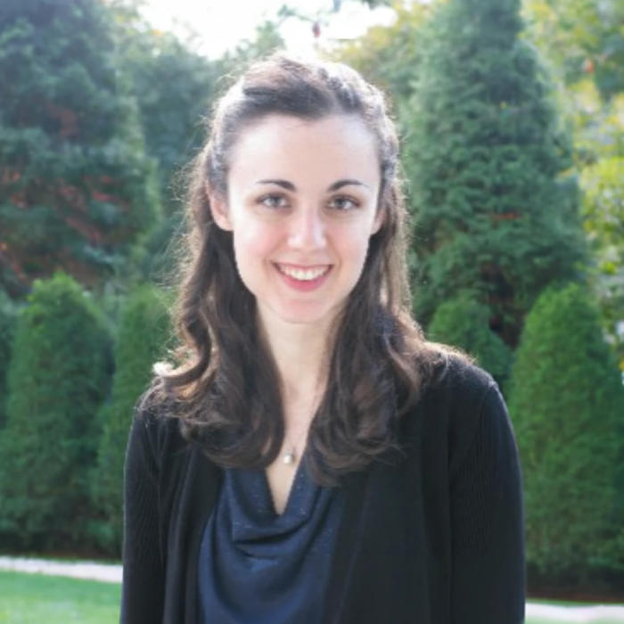 woman standing outside in front of trees smiling at camera
