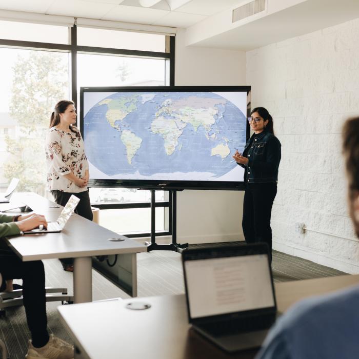 students in a classroom with a professor explaining a map on display