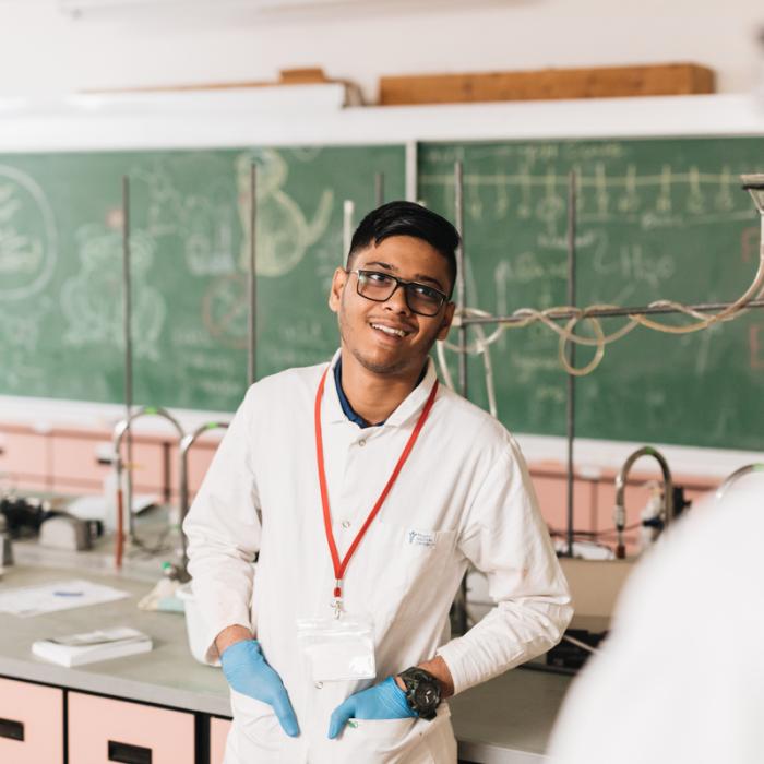student wearing lab coat in lab and smiling 