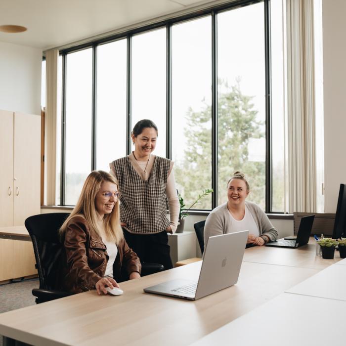 student working on laptop at office with two team members 