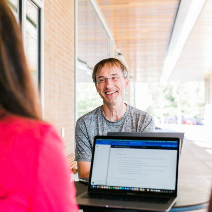 man sitting at table across from woman on laptop