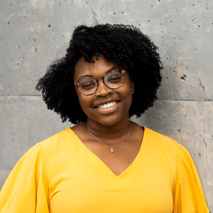 Jenna Louise Palmer-Dyer standing in front of grey wall with yellow shirt