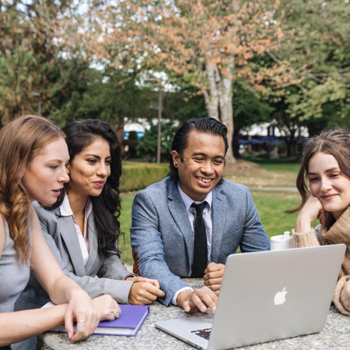 people sitting at a table outside around a laptop