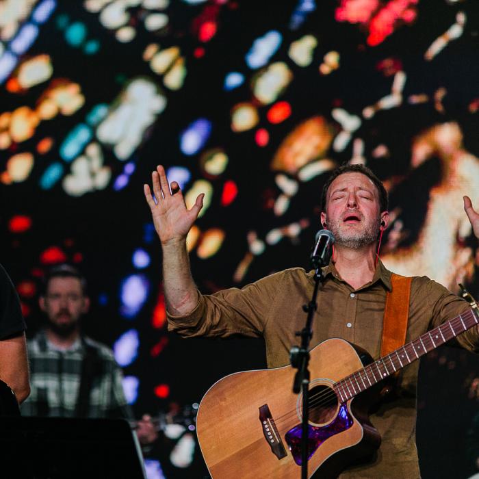 Worship leader with a guitar holding his hands up in praise
