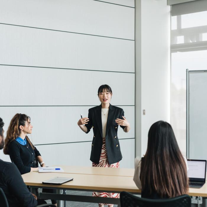 Professionally dressed instructor teaching three students in a white room