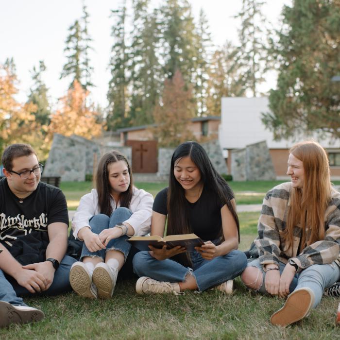 Students sitting in a line on the grass reading a bible together