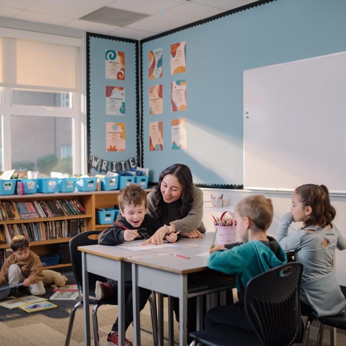 teacher working with students at a desk in a classroom