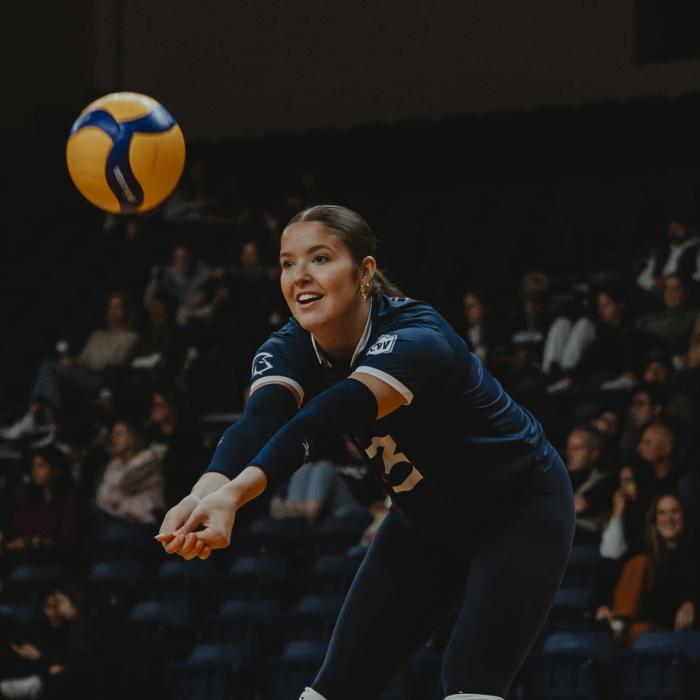 Volleyball player in a dark blue uniform prepares to receive the ball with arms extended.