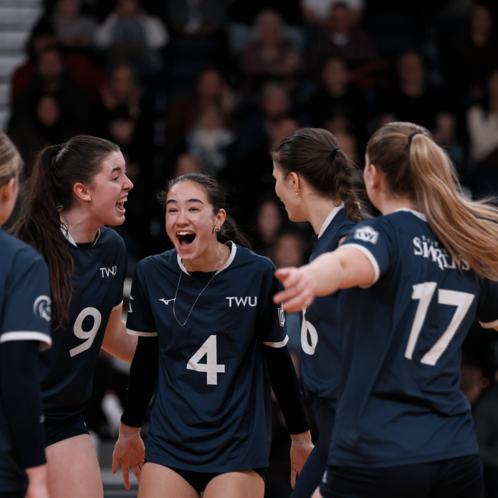  TWU Spartans volleyball players huddle joyfully in blue jerseys.