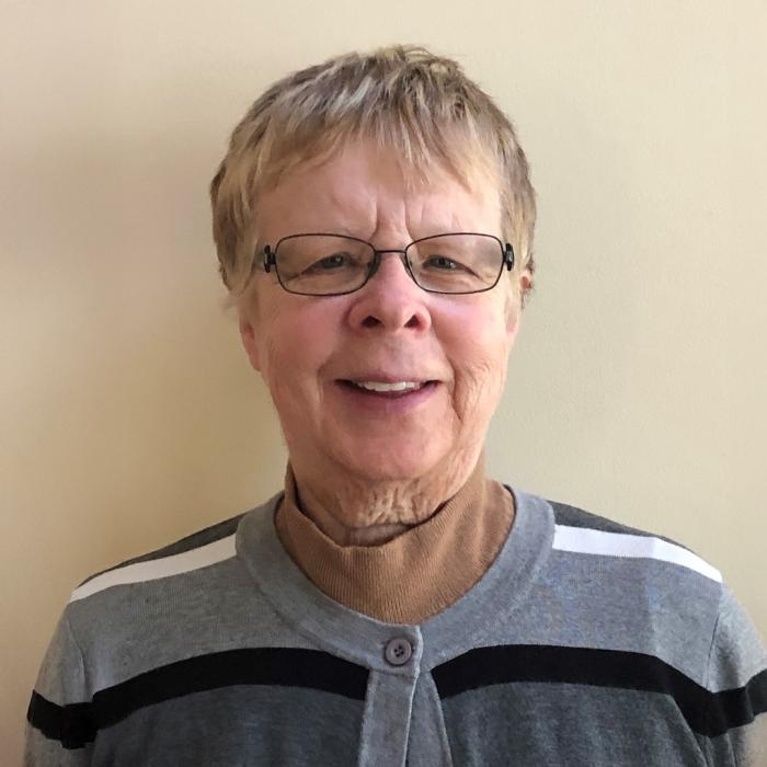 Betty-Jean Tucker with short hair and glasses, wearing a striped sweater.