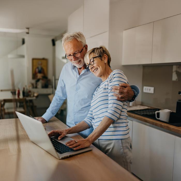 Elderly couple smiling and using laptop at kitchen counter