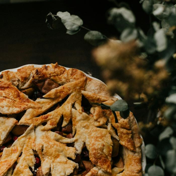 Golden-brown pie with leaf-shaped crust, beside blurred greenery.