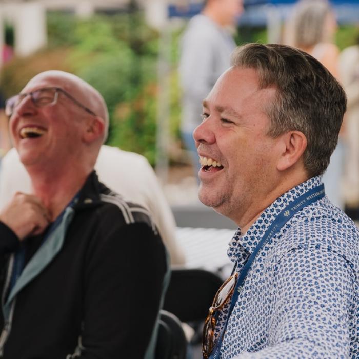 Two men laughing together at an outdoor event.