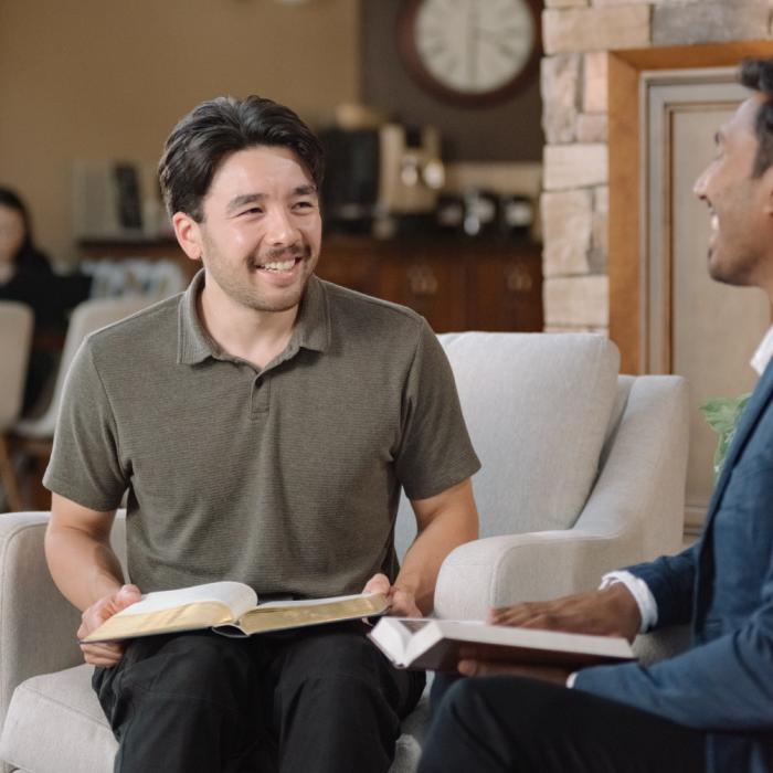 Two men smiling and talking while sitting in a cozy room with open books.