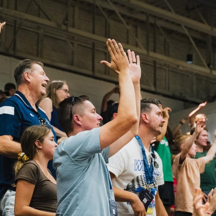 Cheering crowd in a stadium with raised arms, showing excitement and energy.