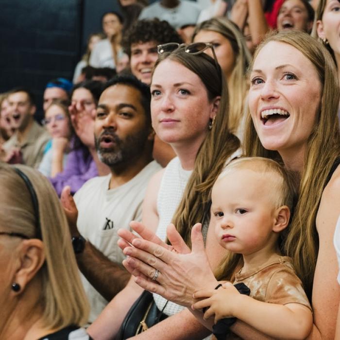 Crowd cheering at an indoor event, mixed ages and expressions of excitement.