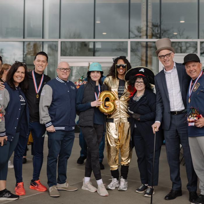 A group of people smiling, some wearing medals, one in a gold outfit, standing outdoors.