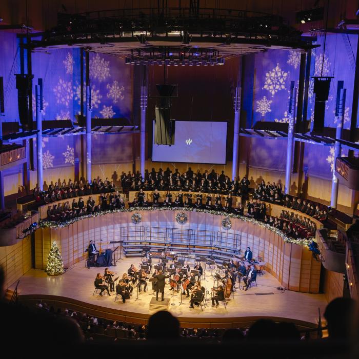Concert hall with orchestra, choir, and blue-lit snowflake decorations.