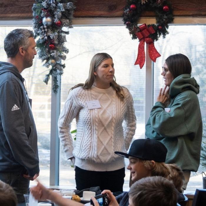 People standing indoors by decorated windows with wreaths.
