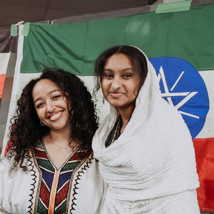 Two people smiling in front of Ethiopian and Ugandan flags.