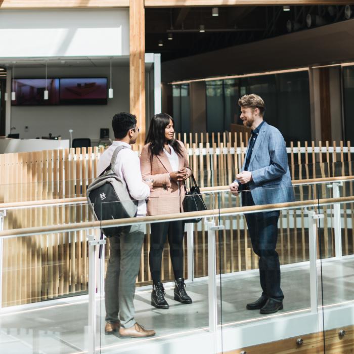 Three people talking in a bright, modern office hallway.