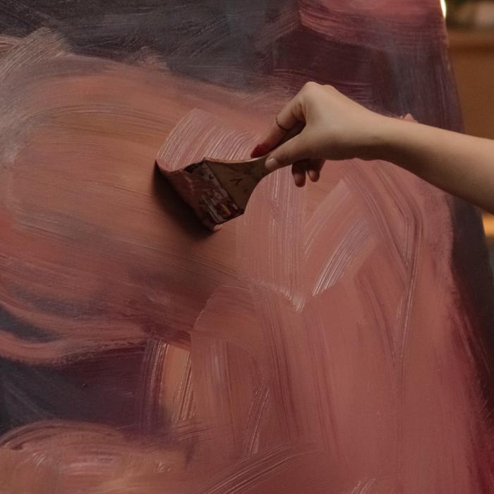 Hand painting large brushstrokes on canvas with earthy tones.