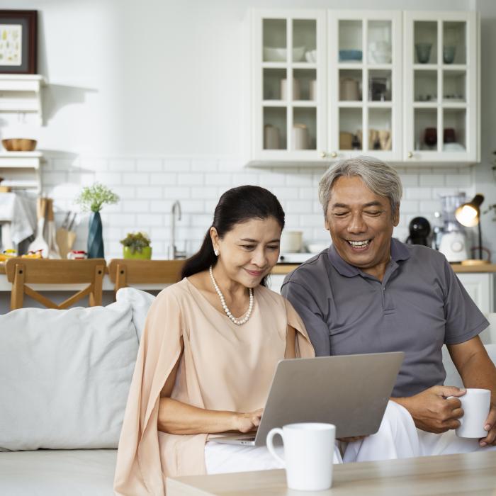 Couple seated on sofa and smiling while looking at laptop