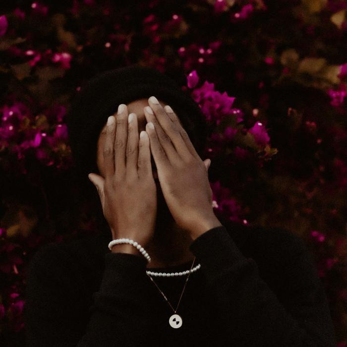 Man covering his face with his hands with a bright pink bush of flowers in the background