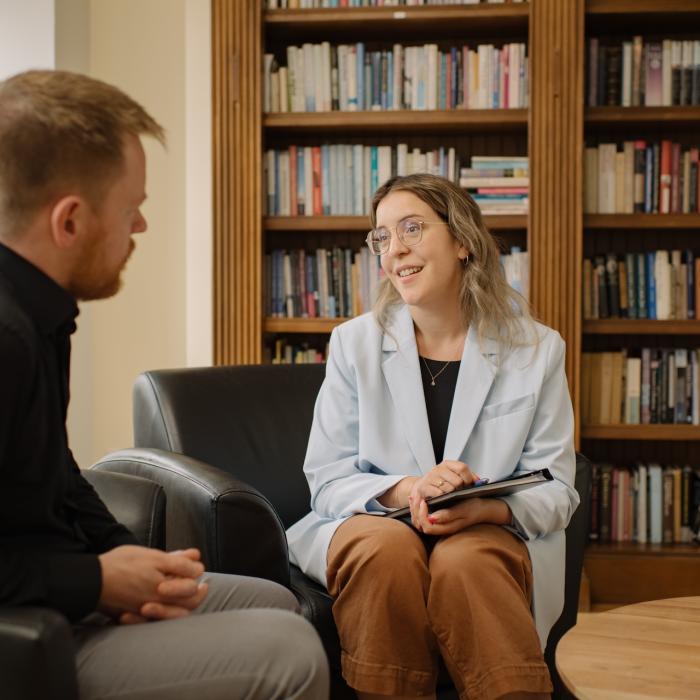 women and man sitting in chairs in front of a bookcase chatting