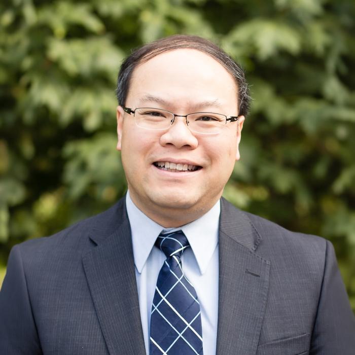 Dr. Herbert Tsang in a suit in front of a tree